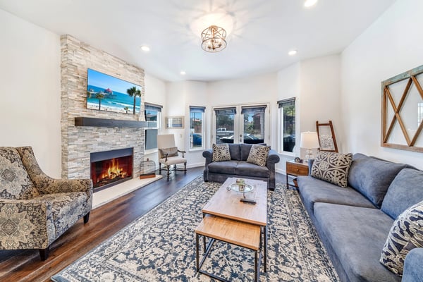 Bright living room with fireplace, multiple sofas, patterned armchairs, wood coffee table, and glass doors overlooking street