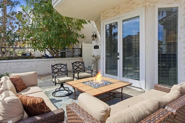 Covered patio with fire table, upholstered seating, metal chairs, and glass doors opening to interior